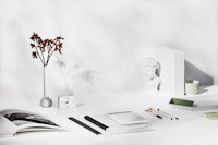 a white desk with books, pens, and a vase